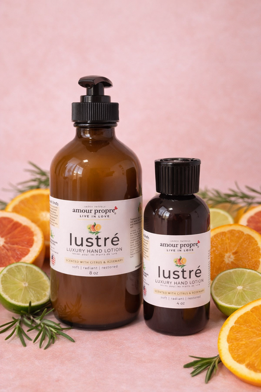 Two bottles of amour propre lustré hand lotion with citrus fruits on a pink background