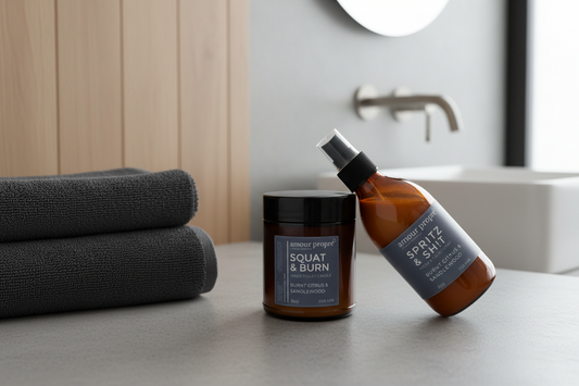 Two brown bottles of King's Throne Toiletries products, one labeled as 'Squat and Burn Candle' and the other as 'Spritz & Sh!t Bathroom Spray FOR HIM'. Both bottles are placed on a white surface against a white background.